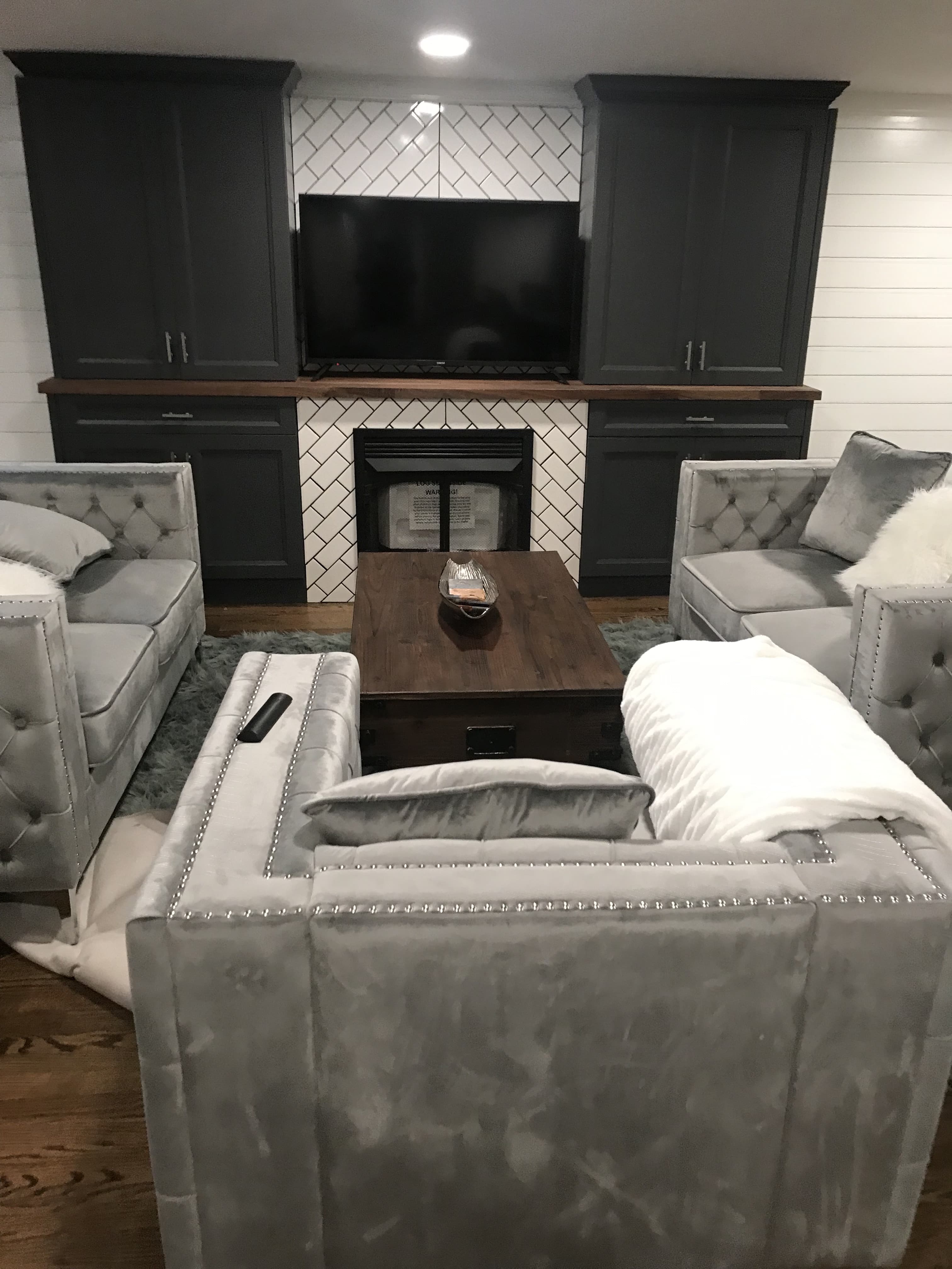 Modern living room with grey velvet tufted sofas, dark built-in cabinets, and a tiled fireplace.